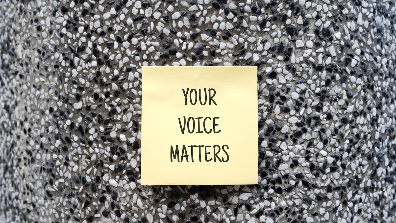 A yellow sticky note that says "Your Voice Matters" on a wall.