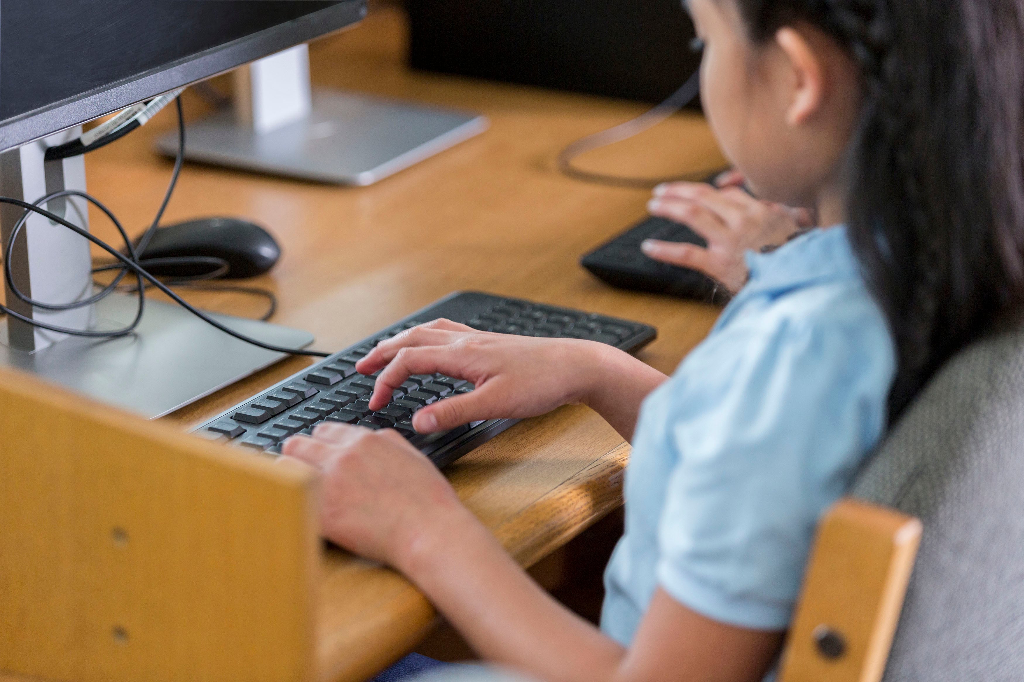 Elementary school girl in computer lab just her hands and side of face showing.
