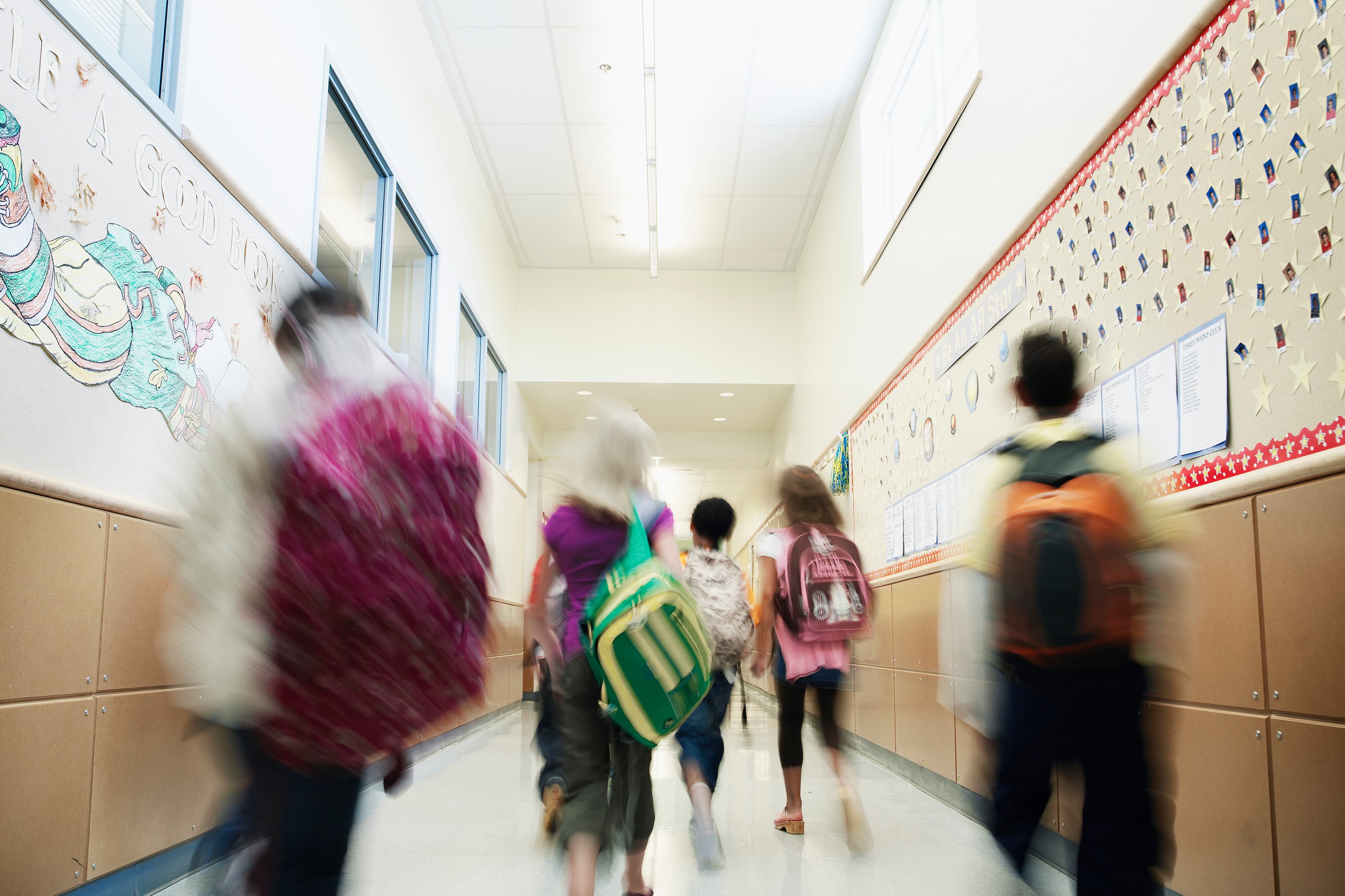 A group of middle school students walk away from the camera in a blurry motion down a school hallway.
