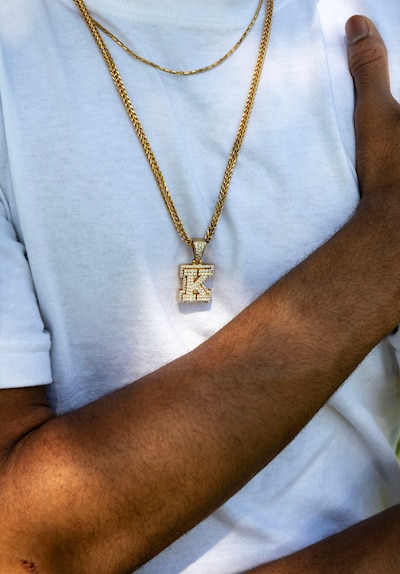 A close up of a white t-shirt with a gold necklace with a diamond letter "K".