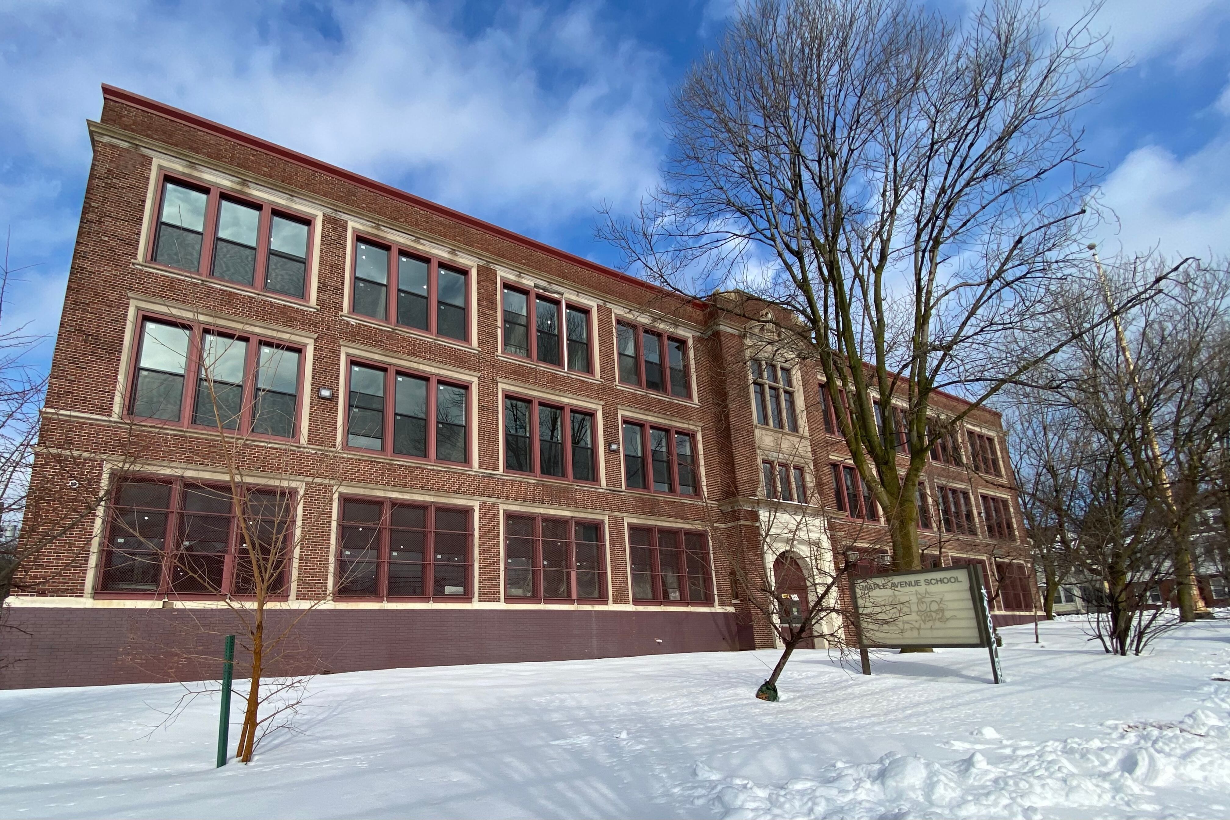 A large stone school building surrounded by snow and a blue sky and clouds in the background.