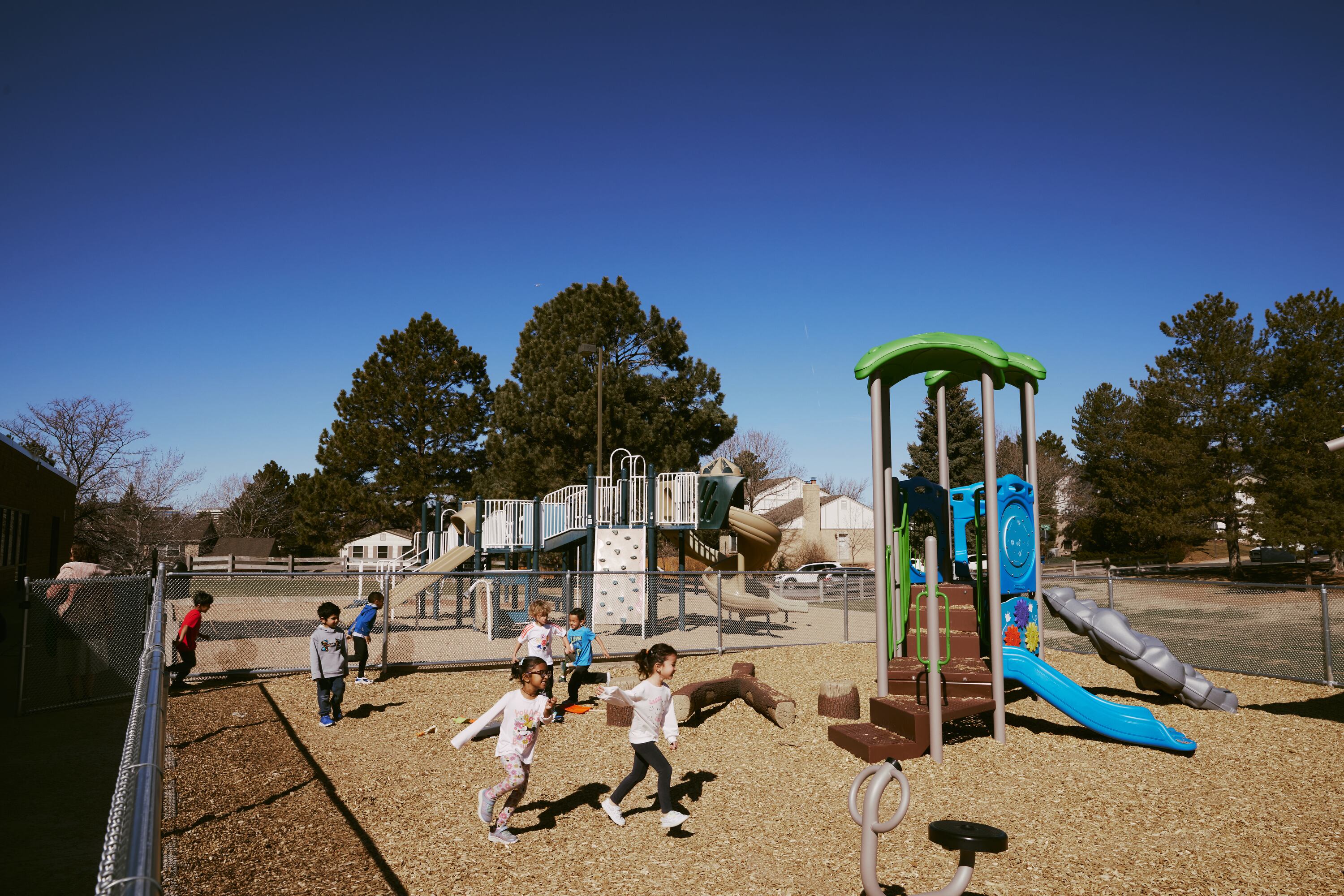Young students play on a playground with a blue sky in the background.