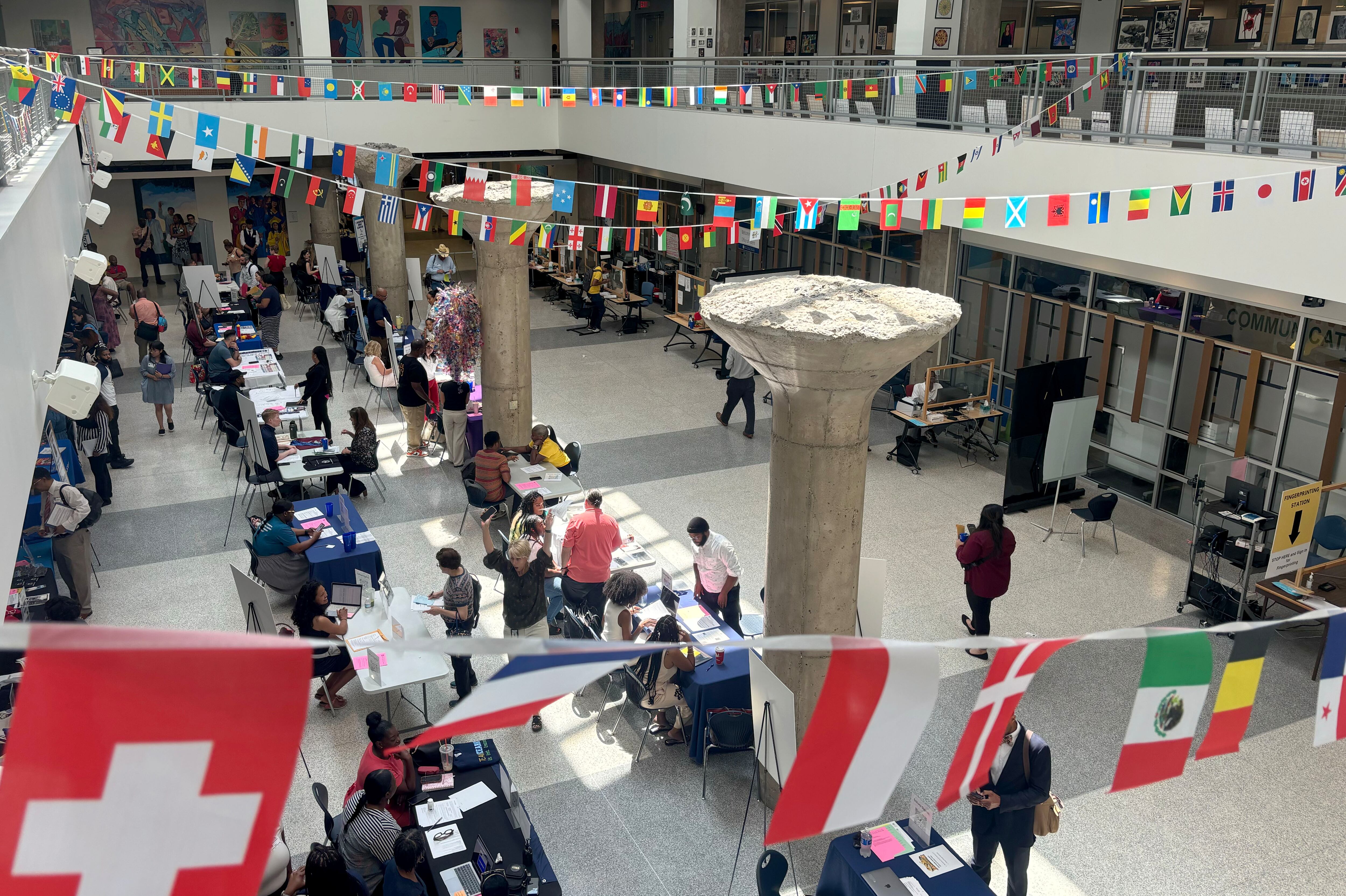 A bird's eye view of a lobby full of people and a string of different countries' flags strung along the top level.